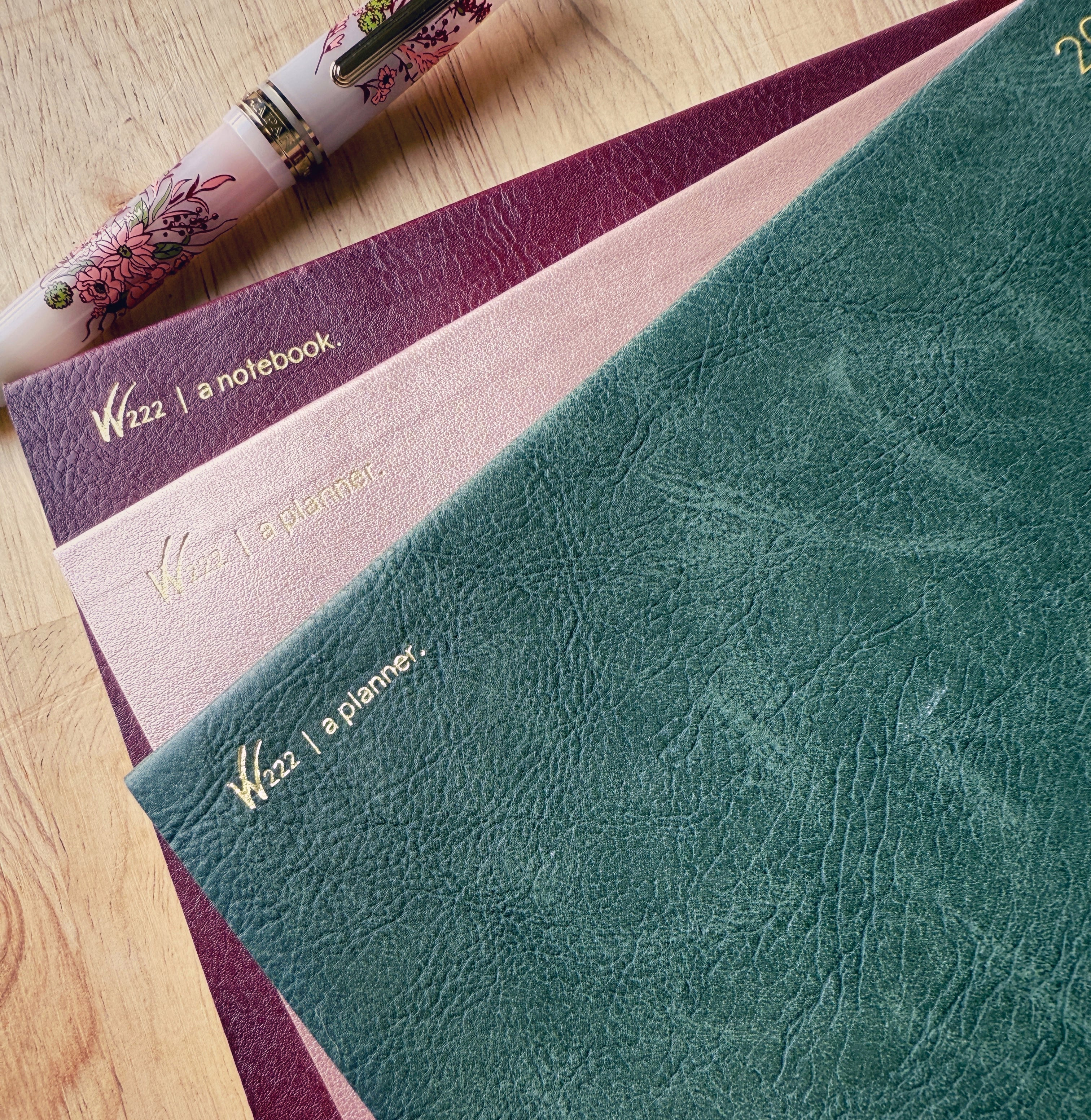 2026 Wonderland 222 planners and notebook.  Alpenglow, North Slope and Lingonberry colors next to a Sailor Pro Gear slim Ancora fountain pen in Vintage Boquet
