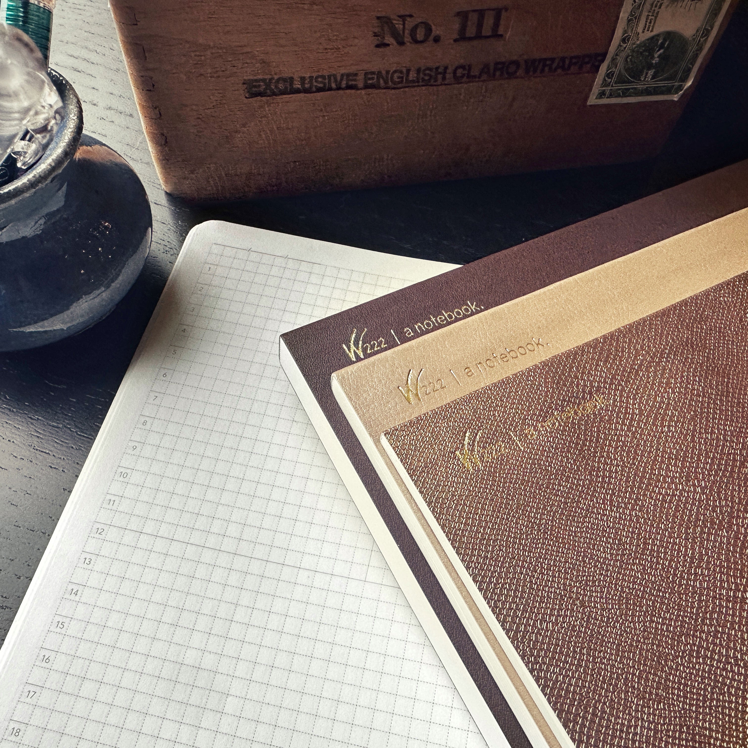 An open Wonderland 222 Tomoe River paper Notebooks.  Tomoe River paper by Tomoegawa.  Notebook open showing grid paper and three notebooks showing various brown and gold colors.  leatherette   texture on the book covers