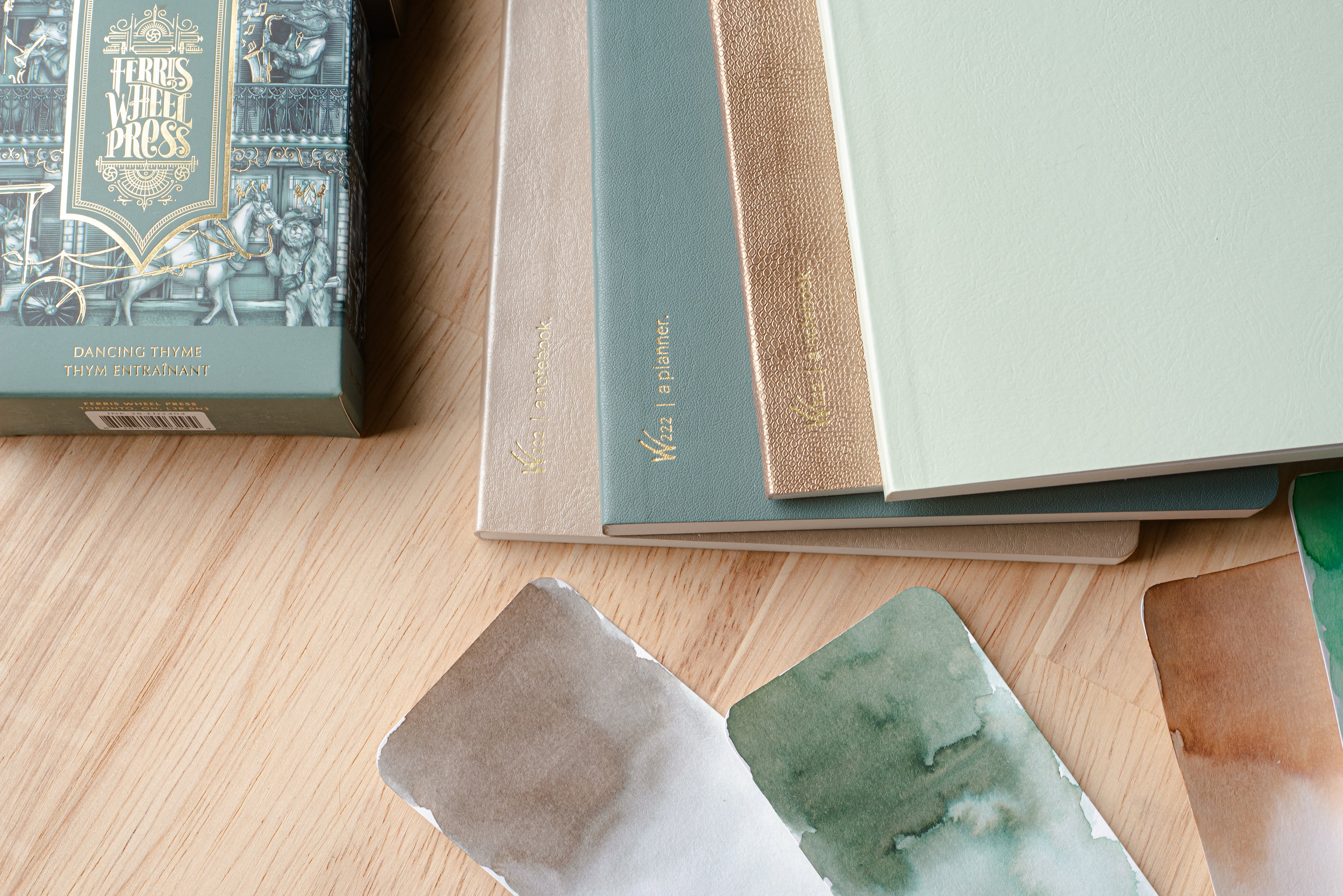 Wonderland 222 planners and notebooks in soft green, gold, and neutral tones styled with Ferris Wheel Press ink and watercolor swatch cards